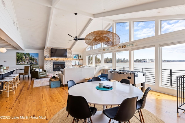 dining space with a fireplace, a ceiling fan, high vaulted ceiling, light wood-type flooring, and beamed ceiling