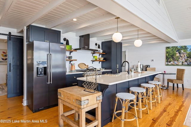 kitchen with a barn door, stainless steel appliances, open shelves, light countertops, and wall chimney exhaust hood