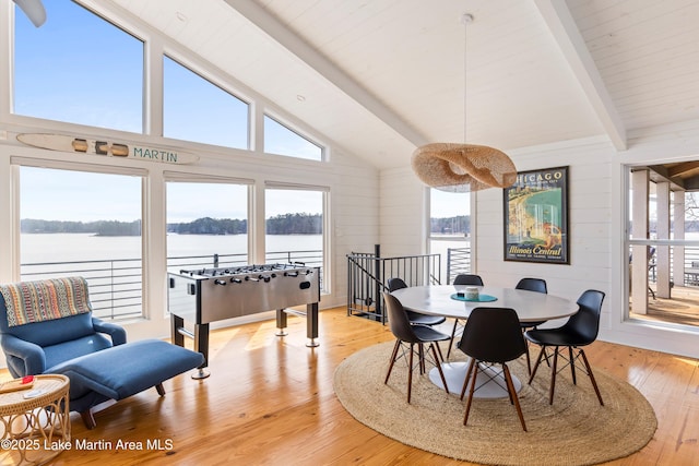 dining area with a water view, light wood-style floors, and vaulted ceiling with beams