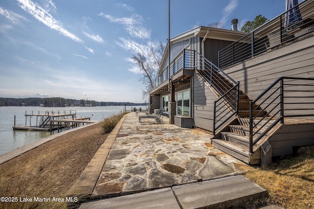 view of home's exterior with a patio, a water view, board and batten siding, a boat dock, and stairs