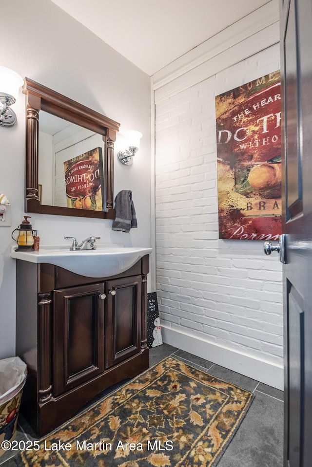 bathroom featuring baseboards, brick wall, and vanity