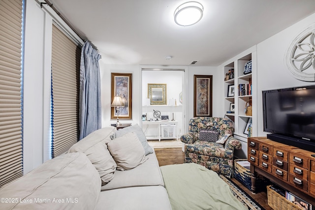 living room with built in features, visible vents, and wood finished floors