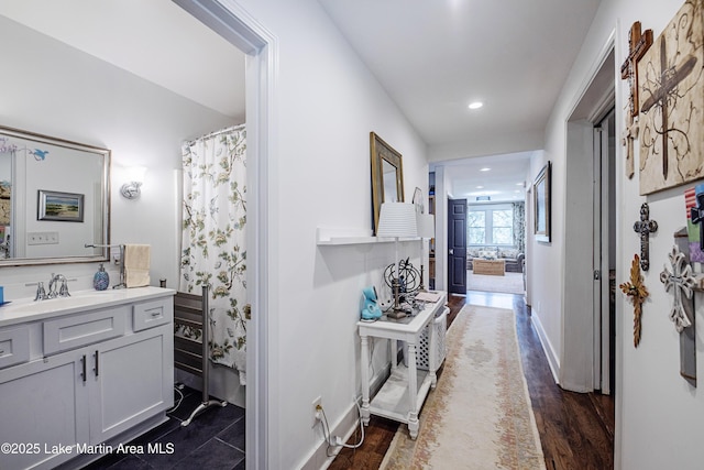 hall with a sink, baseboards, dark wood-type flooring, and recessed lighting