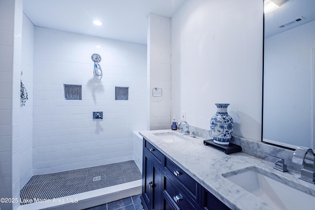 full bath featuring double vanity, visible vents, a tile shower, and a sink