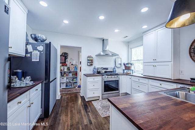 kitchen featuring butcher block countertops, recessed lighting, stainless steel appliances, wall chimney exhaust hood, and dark wood-style flooring