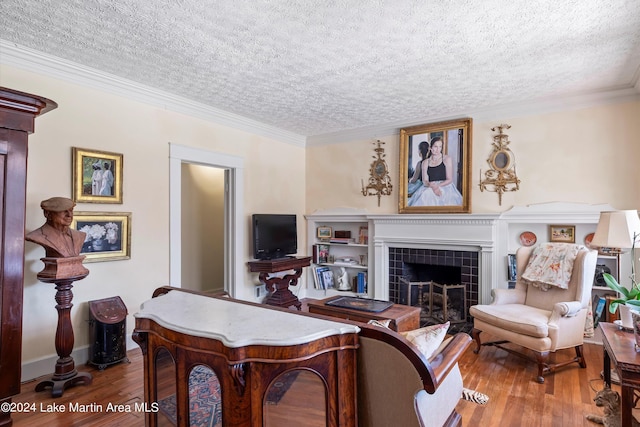 living room featuring crown molding, wood-type flooring, a tile fireplace, and a textured ceiling