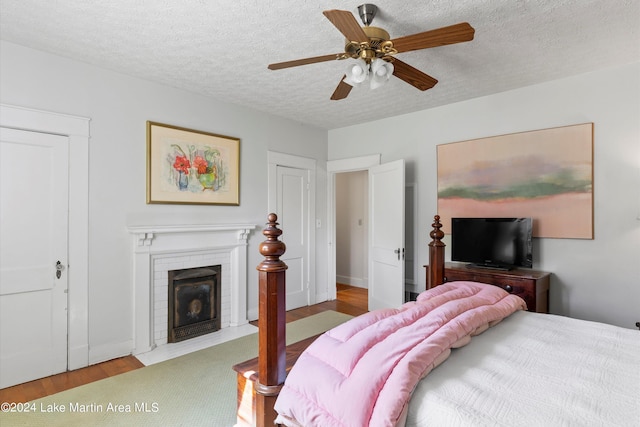 bedroom with ceiling fan, light hardwood / wood-style flooring, a brick fireplace, and a textured ceiling