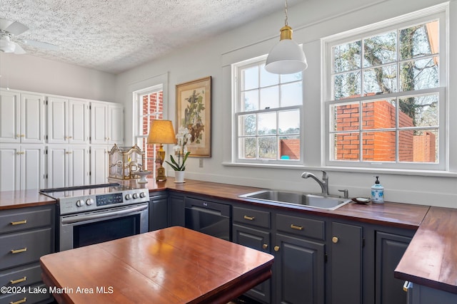 kitchen with wooden counters, hanging light fixtures, sink, and stainless steel range with electric cooktop