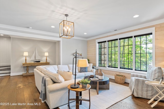 living room with hardwood / wood-style floors, an inviting chandelier, crown molding, and wood walls