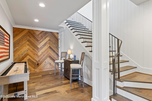 staircase with wooden walls, hardwood / wood-style flooring, and ornamental molding