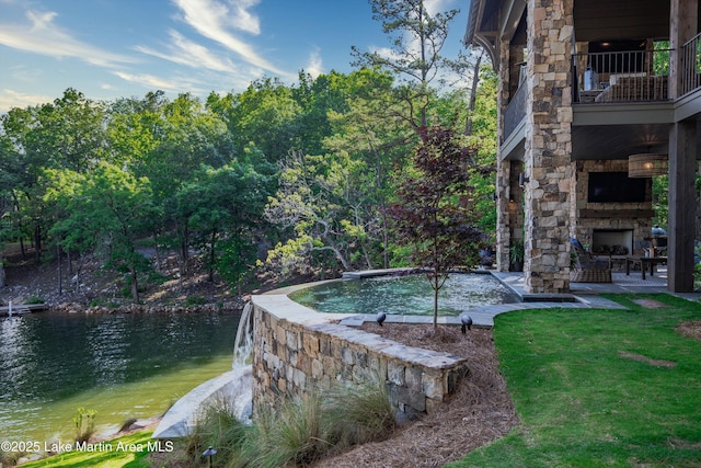 view of pool with a water view and an outdoor stone fireplace