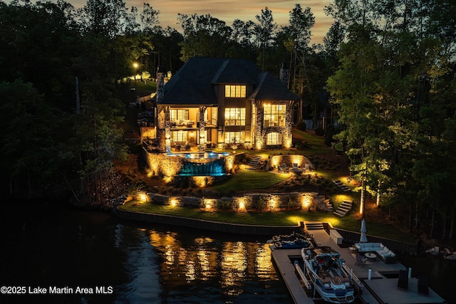 back house at dusk featuring a yard, a balcony, and a water view