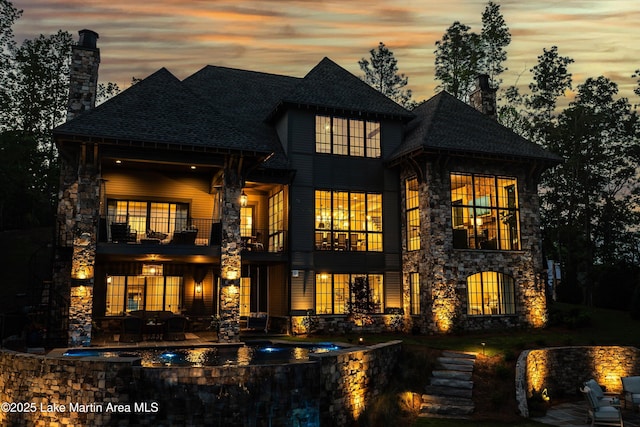 back house at dusk featuring a balcony and a patio area