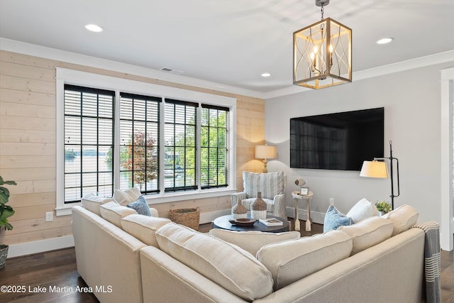 living room featuring dark hardwood / wood-style floors, crown molding, wooden walls, and a notable chandelier