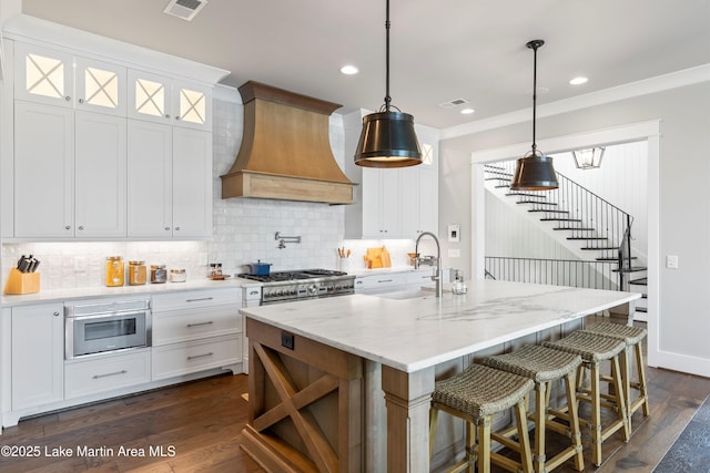 kitchen with white cabinets, custom range hood, a center island with sink, and pendant lighting