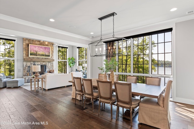 dining area with dark hardwood / wood-style floors, a stone fireplace, crown molding, and an inviting chandelier