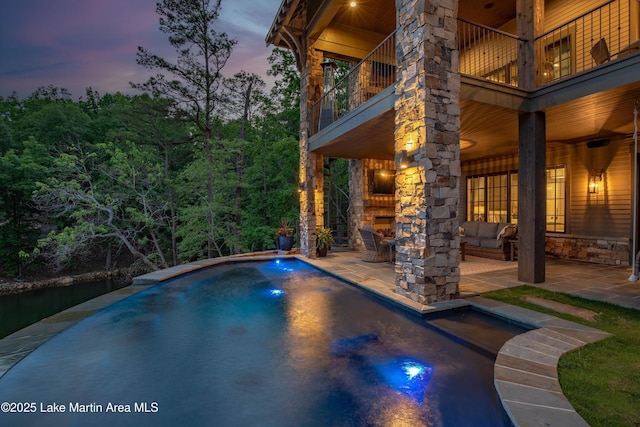 pool at dusk featuring an outdoor living space with a fireplace and a patio area