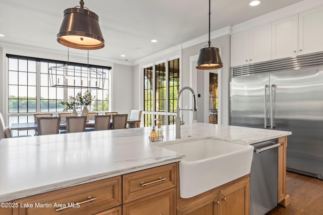 kitchen with light stone countertops, sink, dark wood-type flooring, stainless steel appliances, and decorative light fixtures