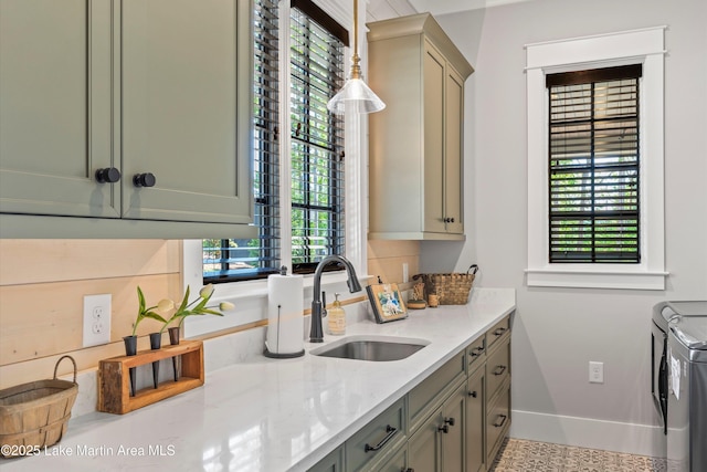 kitchen with washing machine and clothes dryer, sink, a healthy amount of sunlight, light stone counters, and pendant lighting