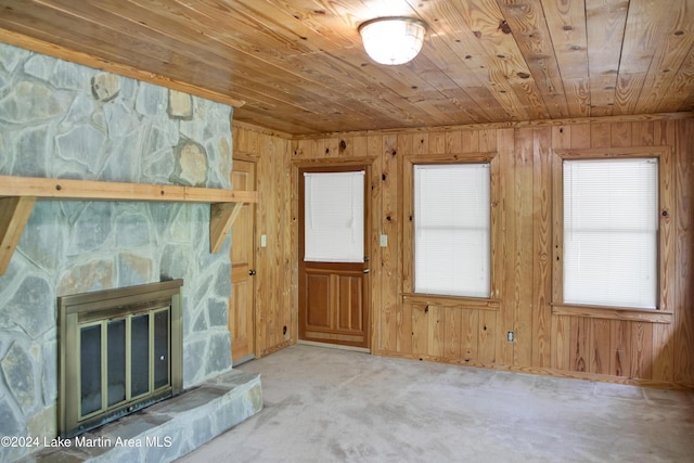 unfurnished living room featuring light colored carpet, wood ceiling, a fireplace, and wooden walls