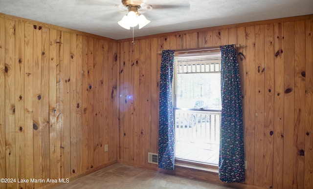 empty room with carpet flooring, wood walls, ceiling fan, and a textured ceiling