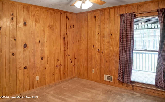 carpeted empty room with wood walls, crown molding, and ceiling fan