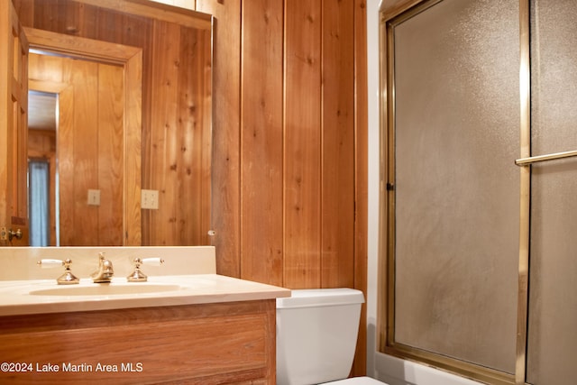 bathroom with wood walls, toilet, vanity, and walk in shower