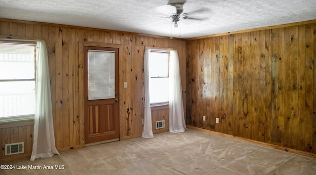 interior space with ceiling fan, a textured ceiling, and wooden walls