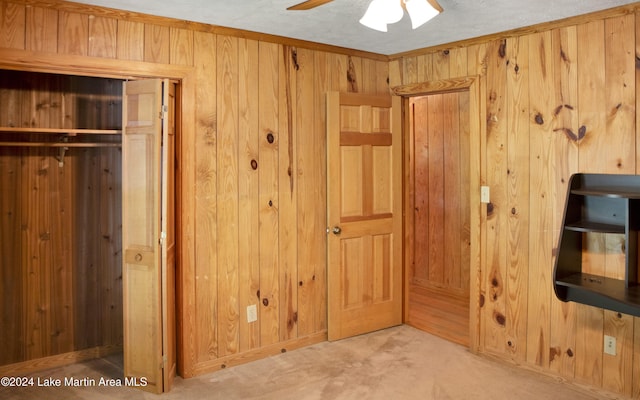 unfurnished bedroom with wooden walls, a closet, ceiling fan, and light colored carpet