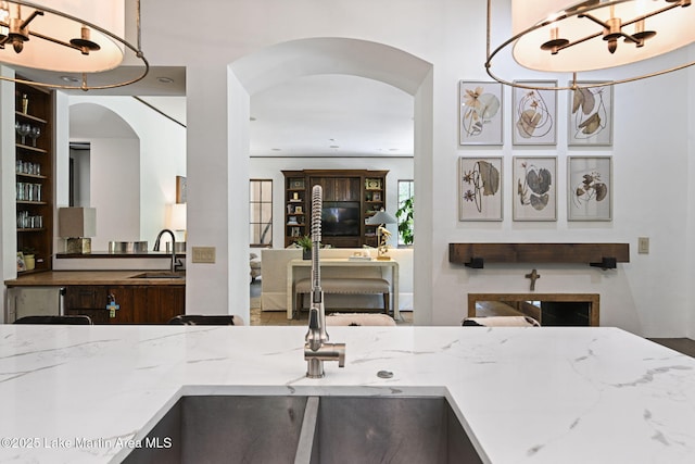 kitchen featuring a sink, a chandelier, arched walkways, and light stone counters