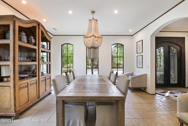 dining area featuring arched walkways, stone tile floors, recessed lighting, crown molding, and a chandelier