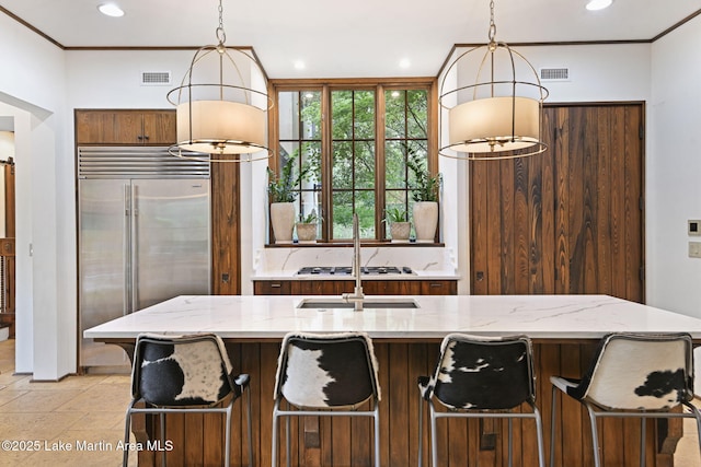 kitchen with built in fridge, hanging light fixtures, recessed lighting, light stone countertops, and crown molding