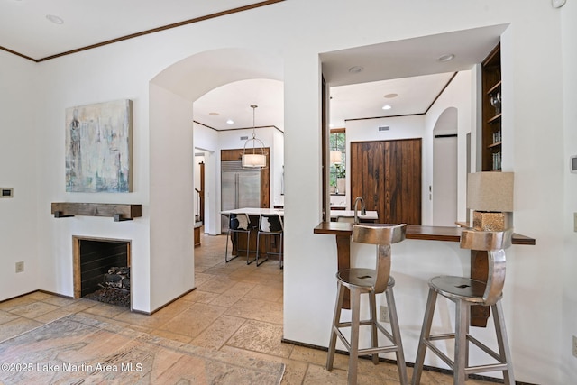 kitchen featuring stone tile floors, arched walkways, built in fridge, a kitchen bar, and a fireplace