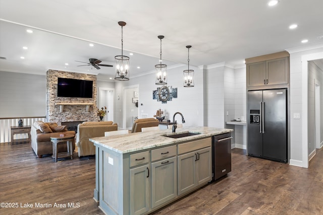 kitchen with sink, a kitchen island with sink, stainless steel appliances, light stone countertops, and decorative light fixtures