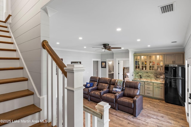 living room featuring crown molding, light hardwood / wood-style floors, ceiling fan, and bar area