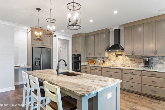 kitchen with pendant lighting, wall chimney range hood, sink, a kitchen island with sink, and black appliances