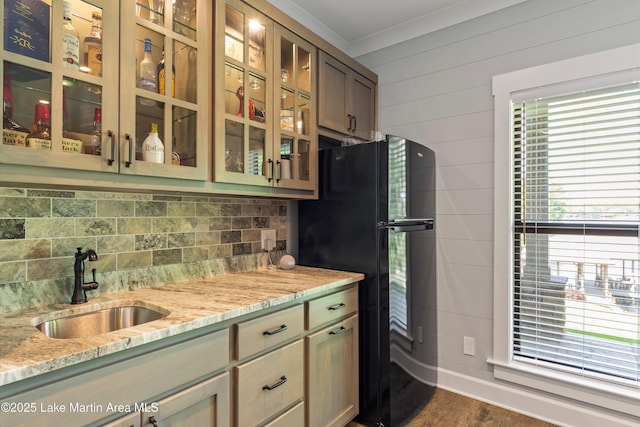 kitchen with sink, black refrigerator, ornamental molding, light stone countertops, and decorative backsplash