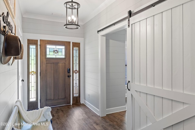 foyer entrance featuring crown molding, a barn door, dark hardwood / wood-style floors, and an inviting chandelier