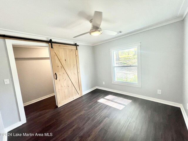 unfurnished bedroom with dark hardwood / wood-style flooring, ceiling fan, crown molding, a barn door, and a closet