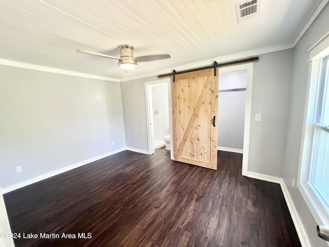 unfurnished bedroom with ceiling fan, dark hardwood / wood-style floors, a barn door, ornamental molding, and connected bathroom