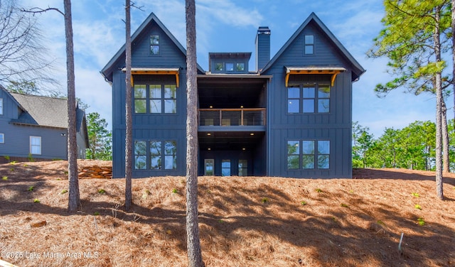 rear view of property featuring a balcony, a chimney, and board and batten siding