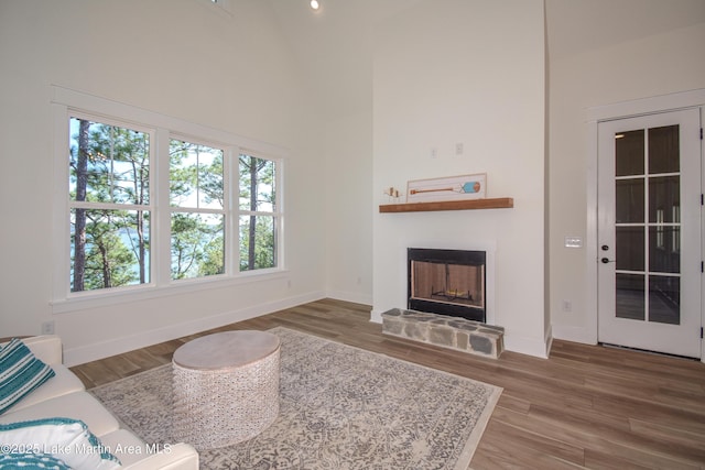 living room featuring a fireplace with raised hearth, a towering ceiling, baseboards, and wood finished floors