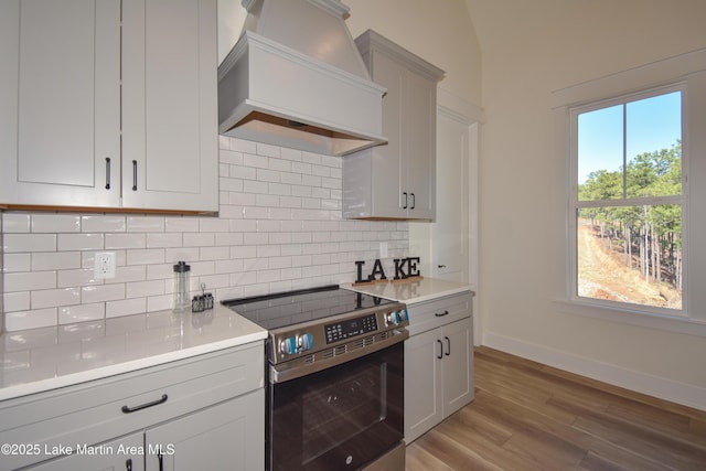 kitchen featuring tasteful backsplash, light countertops, custom range hood, electric range, and light wood-type flooring