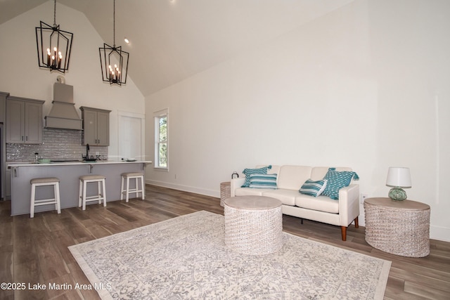 living area with a chandelier, dark wood-type flooring, high vaulted ceiling, and baseboards