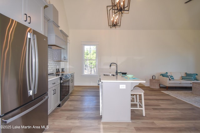 kitchen with a breakfast bar, freestanding refrigerator, premium range hood, a sink, and range with electric stovetop