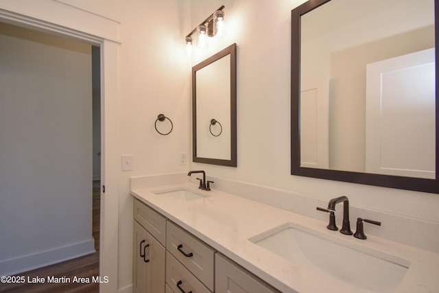 full bath with double vanity, baseboards, a sink, and wood finished floors