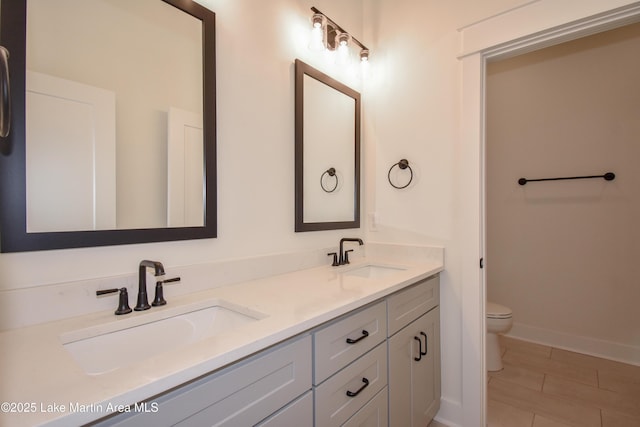 bathroom featuring baseboards, a sink, toilet, and double vanity