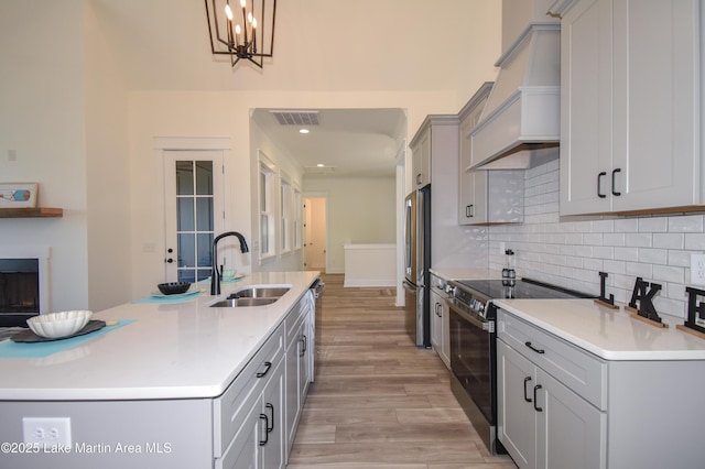 kitchen with a sink, custom exhaust hood, stainless steel appliances, gray cabinetry, and backsplash