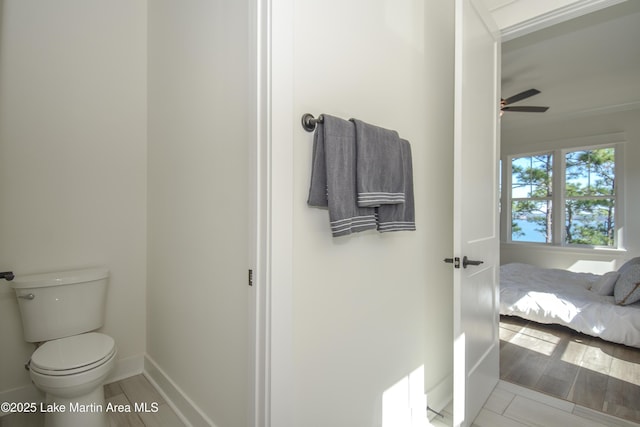 ensuite bathroom with a ceiling fan, wood finished floors, toilet, and baseboards