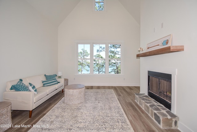 living area with high vaulted ceiling, a fireplace with raised hearth, baseboards, and wood finished floors